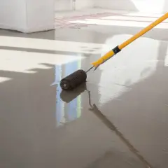 Wylewki anhydrytowe cena za 1m2. Wałek rozprowadza świeżą masę po podłodze z ogrzewaniem podłogowym.