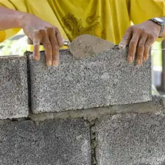 Murarz układa pustaki, sprawdzając ich wymiary. Zaprawa cementowa jest nakładana kielnią.