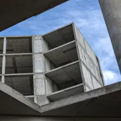 Surowy beton budowy, z widocznymi piętrami i słupami, pod błękitnym niebem. Pianobeton wkrótce nada mu formę.