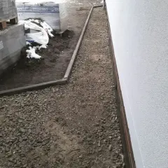 Ułożona opaska przeciwwysadzinowa z kruszywa wokół budynku, obok palety z materiałami budowlanymi.