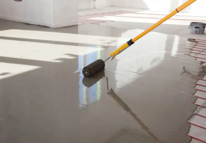 Wylewki anhydrytowe cena za 1m2. Wałek rozprowadza świeżą masę po podłodze z ogrzewaniem podłogowym.