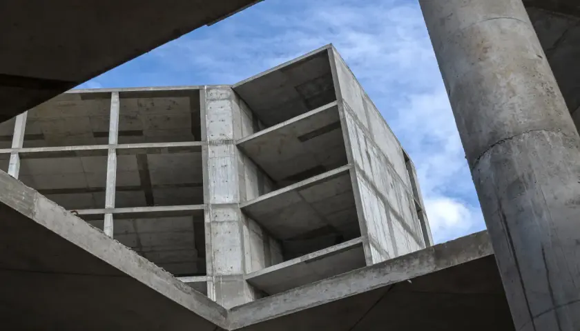 Surowy beton budowy, z widocznymi piętrami i słupami, pod błękitnym niebem. Pianobeton wkrótce nada mu formę.