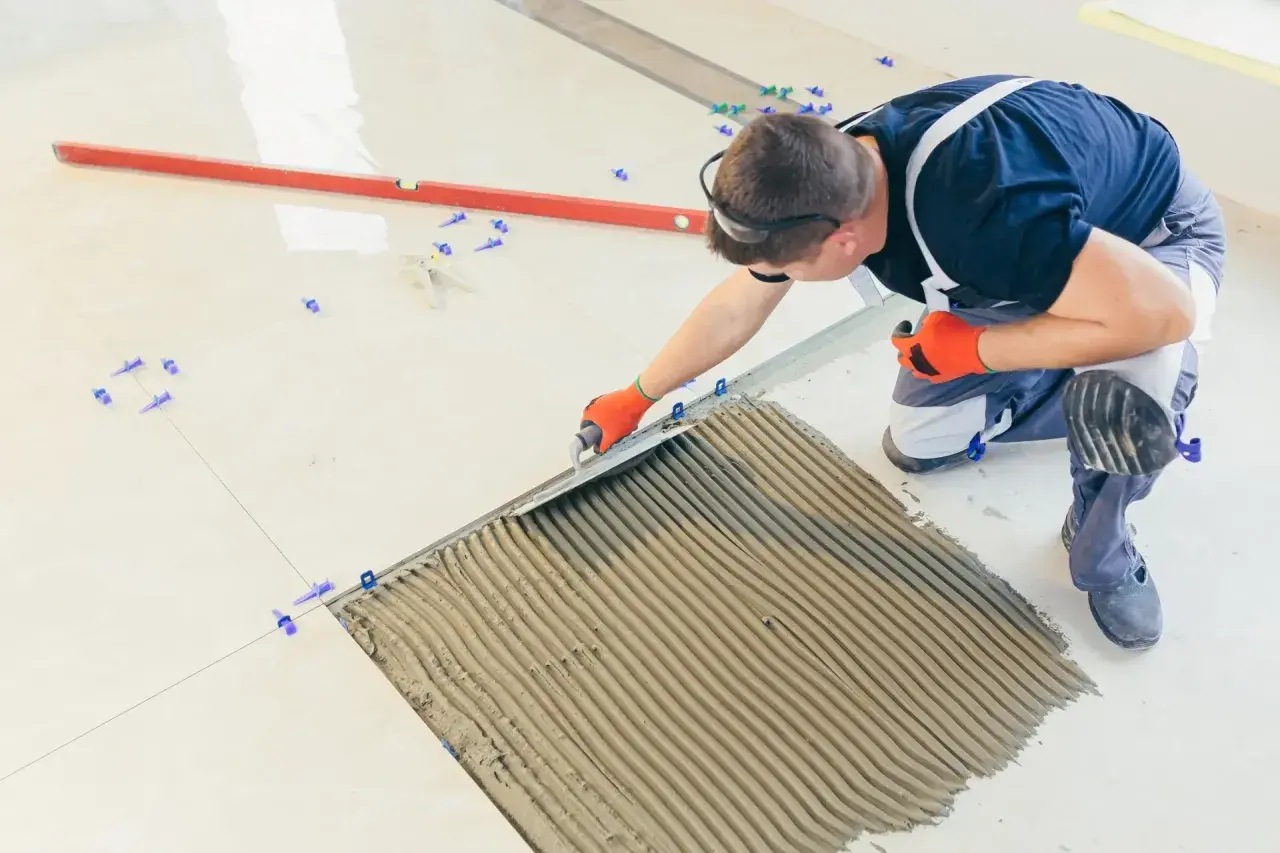 Fachowiec nakłada klej pod płytki 60x30. Precyzyjne układanie to klucz do estetyki i trwałości podłogi.