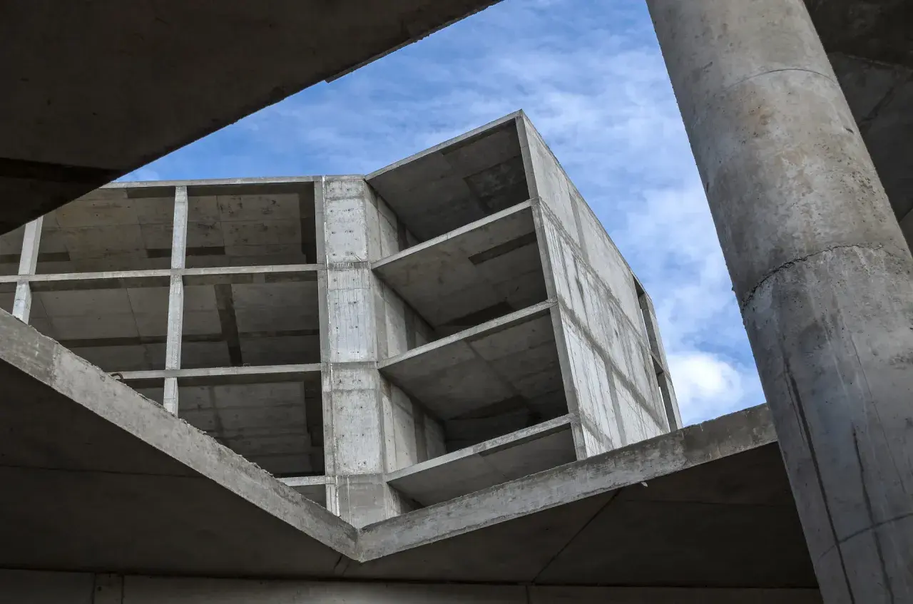 Surowy beton budowy, z widocznymi piętrami i słupami, pod błękitnym niebem. Pianobeton wkrótce nada mu formę.
